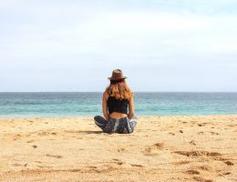 Mulher sentada na areia olhando para praia