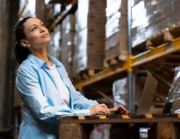 Mulher avaliando um produto no armazém, pensando em como testar um produto antes de investir pesado em produção, com laptop ao lado.