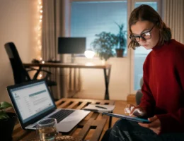 Jovem mulher usando tablet e laptop em um ambiente de home office com iluminação aconchegante, ideal para trabalhar de forma eficiente e confortável