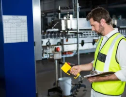 Homem realizando inspeção em máquina industrial em ambiente de fábrica, participando de processos de otimização do layout industrial para melhor uso das máquinas.