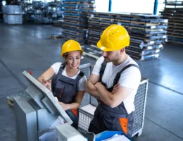 Dose de dois operários em um ambiente de fábrica discutindo causas de paradas não programadas na produção, com destaque para segurança e desempenho.